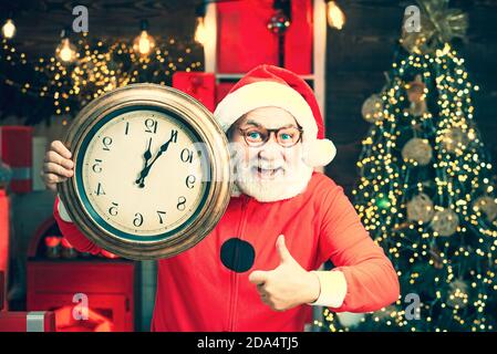 Foto des Weihnachtsmanns mit der Uhr, die fünf Minuten bis Mitternacht zeigt. Portrait von überrascht und lustig Santa. Weihnachtszeit. Frohe Weihnachten. Begrüßung Stockfoto