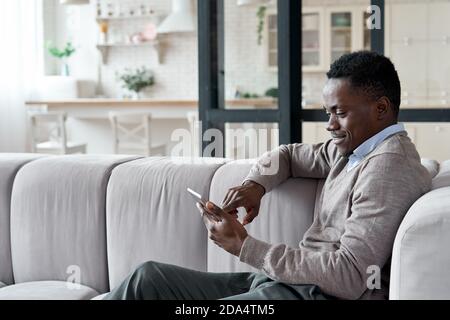 Entspannter afrikanischer Mann mit digitalen Tablet-Apps sitzen auf Couch zu Hause. Stockfoto