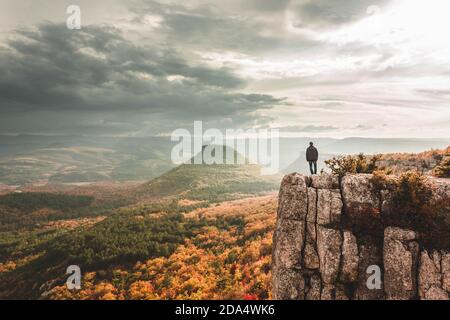 Eine wunderschöne herbstliche Berglandschaft mit einem Mann, der auf der Klippe steht. Vorderansicht von hinten mit Platz für Text Stockfoto
