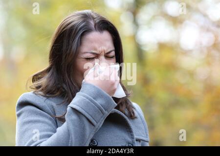 Kranke Frau mit Grippesymptomen, die Gewebe verwendet, um das Gehen zu blasen Im Winter in einem Park Stockfoto