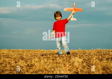 Kleiner netter Junge, der mit einem Spielzeug-Flugzeug spielt. Das Konzept der kindlichen Freundlichkeit und Kindheit. Kinder laufen mit Flugzeug auf dem Feld. Kind spielt mit Modell Stockfoto