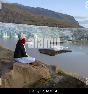 Frau sitzt auf einem Felsen am Ufer, Svinafellsjokull Gletscher, Hornafjorour, Eastern Region, Island Stockfoto