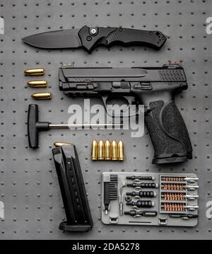 Eine Pistole, Patronen dafür und ein Klappmesser auf dunklem Hintergrund. Selbstverteidigungs- und Überlebenskit. Kompakte kantige Waffen und Schusswaffen. Stockfoto