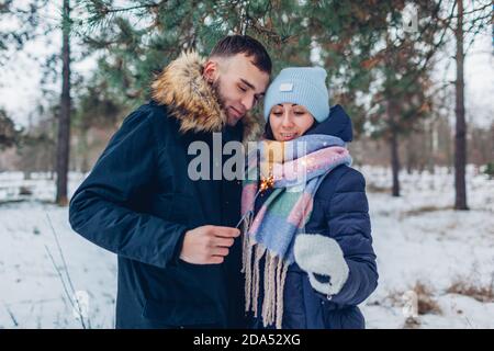 Junge liebevolle Paar brennende Wunderkerzen im Winterwald. Weihnachten und Neujahr Feier. Menschen, die Spaß im Freien haben Stockfoto