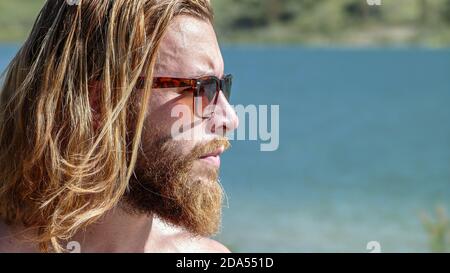 Blonde junge Mann mit Sonnenbrille Blick auf den Horizont von Ein See Stockfoto