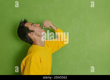 Junger Mann trinkt Olivenöl in einer kleinen Plastikampulle auf grünem Hintergrund, Konzept eines gesunden Lebensstils Stockfoto