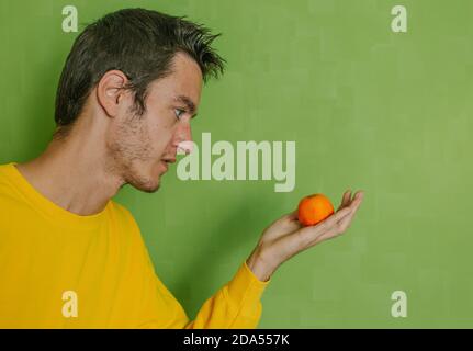 Junger Mann mit Mandarine orange in der Hand auf einem grünen Hintergrund, Diät-Konzept Stockfoto