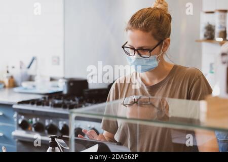 Blonde Kellnerin trägt Gesichtsmaske arbeiten in einem Café. Stockfoto