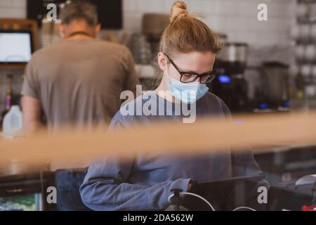 Blonde Kellnerin trägt Gesichtsmaske arbeiten in einem Café. Stockfoto