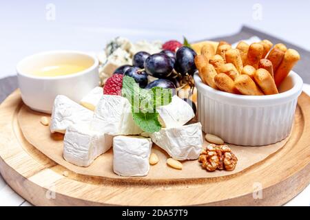 Brett mit verschiedenen Käsesorten. Käse Mischung Set dor blu chedar Parmesan Brie Honig Sauce Fingerbrot und Trauben auf Wooren Parte. Frühstücksteller auf der Speisekarte des Restaurants. Gesundes Snacksortiment Stockfoto