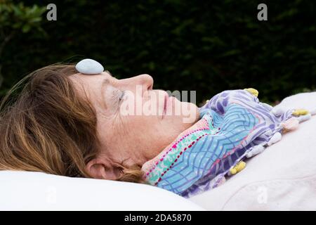 Frau mit Stein auf der Stirn während einer alternativen Therapie in einem Garten. Stockfoto