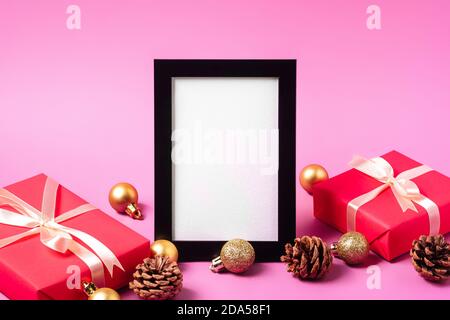 Weihnachten minimale Komposition mit leerem Bilderrahmen. Goldenes Ornament, Geschenkboxen und Tannenzapfen Dekorationen. Vorlage für Grußkarten Stockfoto
