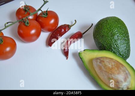 Zutaten für Guacamole auf weißem Hintergrund. Kirschtomaten, Chilischoten, Avocados, Zutaten für mexikanisches Essen. Stockfoto