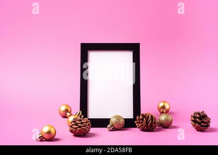 Weihnachten minimale Komposition mit leerem Bilderrahmen. Goldenes Ornament, Tannenzapfen Dekorationen. Vorlage für Grußkarten Stockfoto