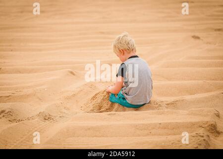 Shot von einem Kind mit schönen Haaren spielen in der Sand mit dem Rücken zur Kamera Stockfoto