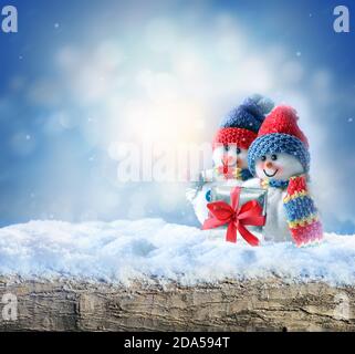Zwei lustige Schneemänner mit Geschenkbox im Winter auf dem Schnee. Urlaubskonzept. Stockfoto