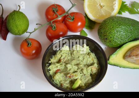 Eine köstliche Schüssel Guacamole neben frischen Zutaten auf einem Tisch mit Tortilla-Chips und Salsa. Sandwich mit Guacamole, roter Paprika, Limette, Zitrone Stockfoto