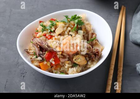 Gebratener Reis mit Meeresfrüchten, Gemüse, Ingwer und Petersilie auf dunklem Hintergrund. Asiatische Küche. Vegetarisches Essen Stockfoto