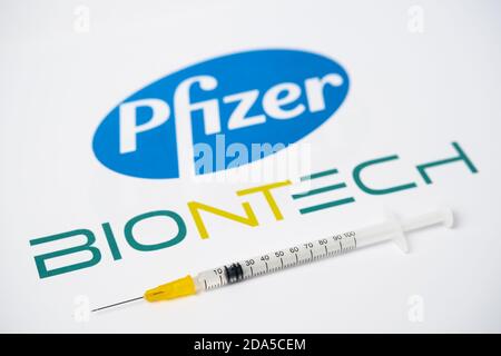 Stafford / Großbritannien - 9. November 2020: Pfizer BioNTech Covid-19 Impfstoffkonzept. Spritze auf einer Fingerspitze balanciert und verschwommene Firmenlogos auf Th Stockfoto