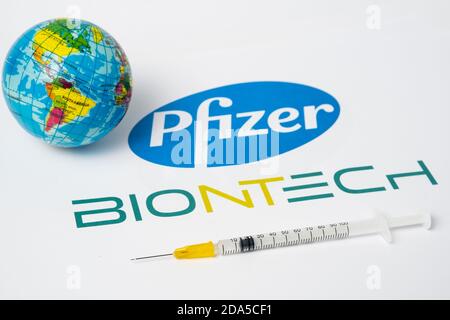 Stafford / Großbritannien - 9. November 2020: Pfizer BioNTech Covid-19 Impfstoffkonzept. Spritze und eine verschwommene Spielzeugkugel mit verschwommenen Firmenlogos auf t Stockfoto