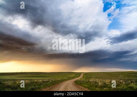 Unbefestigte Straße durch sanfte Hügel mit Sturmwolken im Thunder Basin National Grassland, Wyoming, USA
