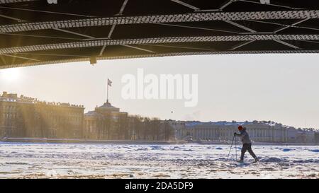 Silhouette des Skifahrers auf dem Eis der gefrorenen Neva Fluss unter der Palastbrücke im Winter bei Sonnenuntergang Stockfoto