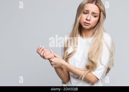 Ungesunde junge Frau hält ihr schmerzhaftes Handgelenk, leidet unter Schmerzen in der Hand, trauriges Aussehen. Karpaltunnelsyndrom, Arthritis, neurologische Erkrankung concep Stockfoto