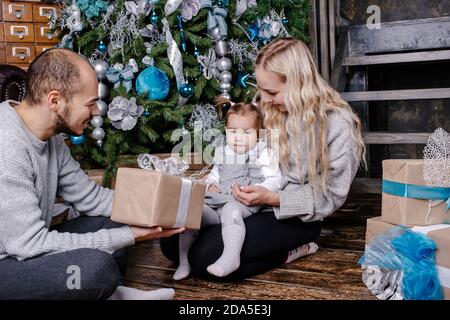 Glückliche Eltern schenken einem Kind vor dem Weihnachtsbaum ein Weihnachtsgeschenk. Feiertage, Geschenke, weihnachten, Weihnachten, Geburtstagskonzept. Stockfoto