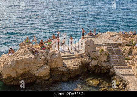 Junge Erwachsene feiern auf Sonnenuntergang am felsigen Strand in Rovinj, Kroatien. Stockfoto