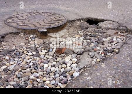 Zerstörte Asphaltstraße, Loch neben Sanitärinstallschacht Stockfoto