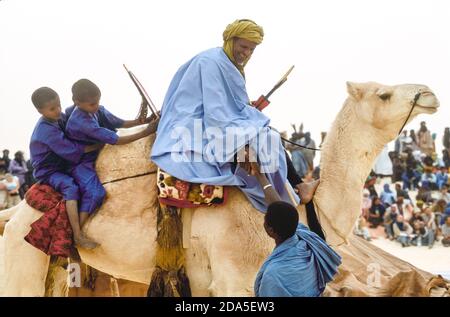 Afrika, Mali, Essakane, in der Nähe von Timbuktu. Tuareg-Mann mit zwei kleinen Jungen auf seinem Kamel grüßt einen Freund. Festival in der Wüste, Festival au Desert 2005 Stockfoto