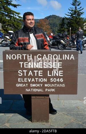 Random Clean Cut Biker steht beim Nationalpark rustikal Holzschild am Straßenrand, das die Bundesstaaten North Carolina und Tennessee kennzeichnet Line in der Great Smoky Stockfoto