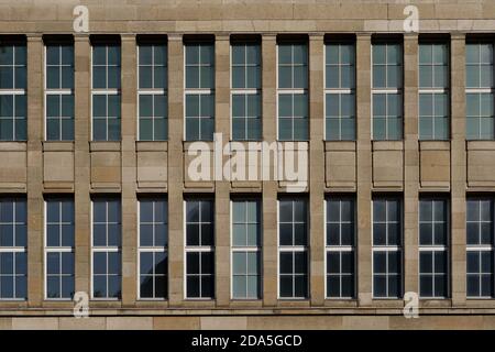 Vorderansicht der modernen Fassade mit cremebraunen rauen Granitsteinfliesen und hohen Fenstern auf symmetrischem rechteckigem Muster. Stockfoto
