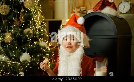 Kid Santa Claus genießen in serviert Lebkuchen Kuchen und Milch. Weihnachtsmann essen Kekse und Milch trinken am Heiligabend. Frohes neues Jahr. Stockfoto