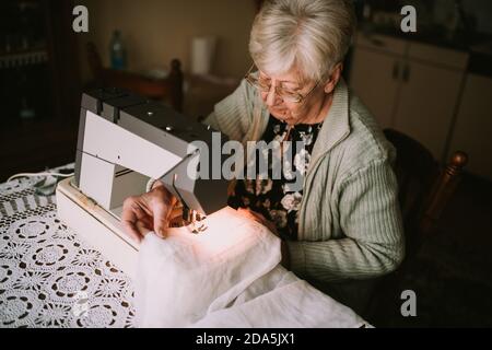 Draufsicht auf eine Großmutter, die auf einer Maschine im Wohnzimmer näht. Pensionierte Näherin Stockfoto
