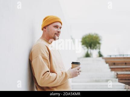 Portrait von stilvollen Mann Hipster in gelben Hut mit Papier tasse Kaffee in der Stadt Stockfoto
