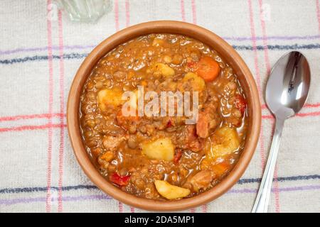 Tonschüssel mit hausgemachtem Linseneintopf, Tomate, spanischem Chorizo, Fleisch und Kartoffeln auf einer Tischdecke Stockfoto