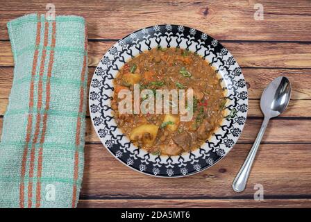 Köstliche hausgemachte Eintopf mit Linsen, Tomaten, spanischen Chorizo, Fleisch und Kartoffeln serviert in einem tiefen Teller mit einem schwarzen Muster auf einem Holzbrett mit einem TL Stockfoto