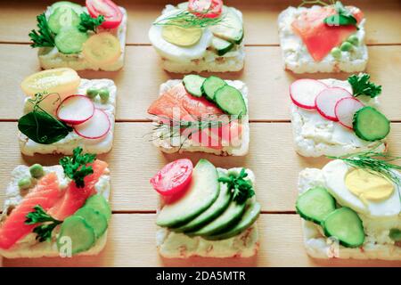 Gesunde Sandwiches mit Reis knusprigem Brot und verschiedenen Belägen. Gesunde Zutaten für das Abendessen beginnen. Vorspeisen auf einem Holztisch. Geräucherter Lachs und Avocado Sandwiches. Frische Zutaten. Stockfoto