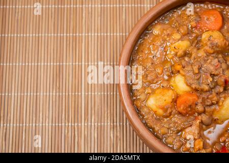 Tonschüssel mit hausgemachtem Linseneintopf, Tomate, spanischem Chorizo, Fleisch und Kartoffeln auf einer Tischdecke Stockfoto