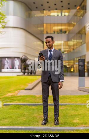 In voller Länge Aufnahme von afrikanischen Geschäftsmann stehen im Freien und mit Telefon Stockfoto