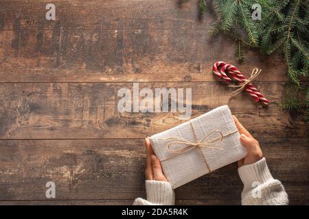 Geschenkbox für Weihnachten. Frau Hände in weißen Pullover auf Holztisch halten Weihnachten Geschenk-Box - Draufsicht mit Copy Space Stockfoto