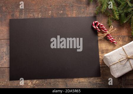 Mockup Weihnachtskarte mit Baum und Geschenk, Flatlay auf rustikalem Holzhintergrund, mit Platz für Ihren Text auf schwarzem Papier Stockfoto