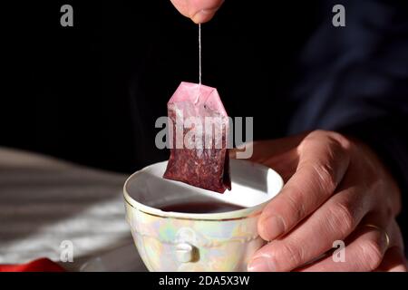 Teebeutel mit einer Tasse Tee in den Händen beim Mann/Closeup Stillleben Lebensmittelfotografie/frische rote Kräuterbecher Tee Stockfoto