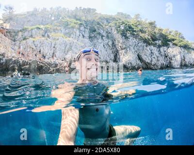 Lächelnder Mann, der im Meer schwimmt und ein Foto von sich selbst macht, an einem sonnigen Sommertag. Capri Island, Italien. Stockfoto