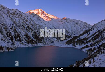 Majestätischer Berggipfel steigt über dem See in den letzten Strahlen der untergehenden Sonne; Hochland in der Wintersaison bei Sonnenuntergang Stockfoto