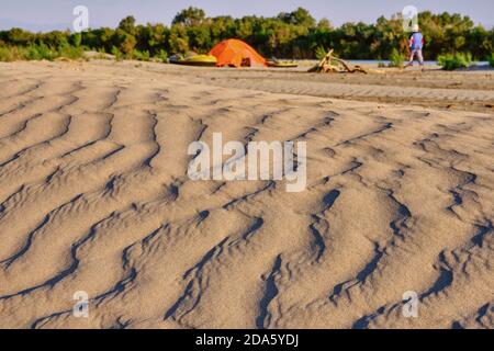 Textur von Sanddünen im weichen Licht der Untergehende Sonne auf dem Hintergrund eines Feriencamps mit Boote und ein Lagerfeuerplatz Stockfoto