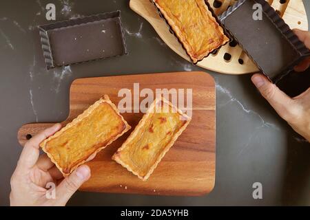 Hand Holding a Square Shaped Tart Mold and Fresh Baked Pumpkin Tartlet Placing on the Wooden Breadboard Stockfoto