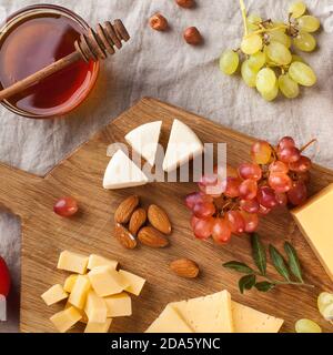 Käseplatte. Verschiedene Käsesorten auf einem Holzbrett mit Trauben, Honig, Nüssen auf einem Leinentischtuch. Stockfoto