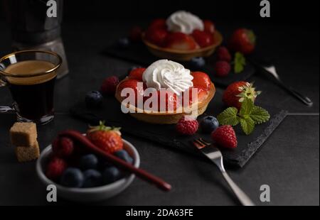 Hausgemachte Bio-Erdbeerkuchen mit Himbeere und blauer Beere mit einem Kaffee auf dunklem Hintergrund. Stockfoto